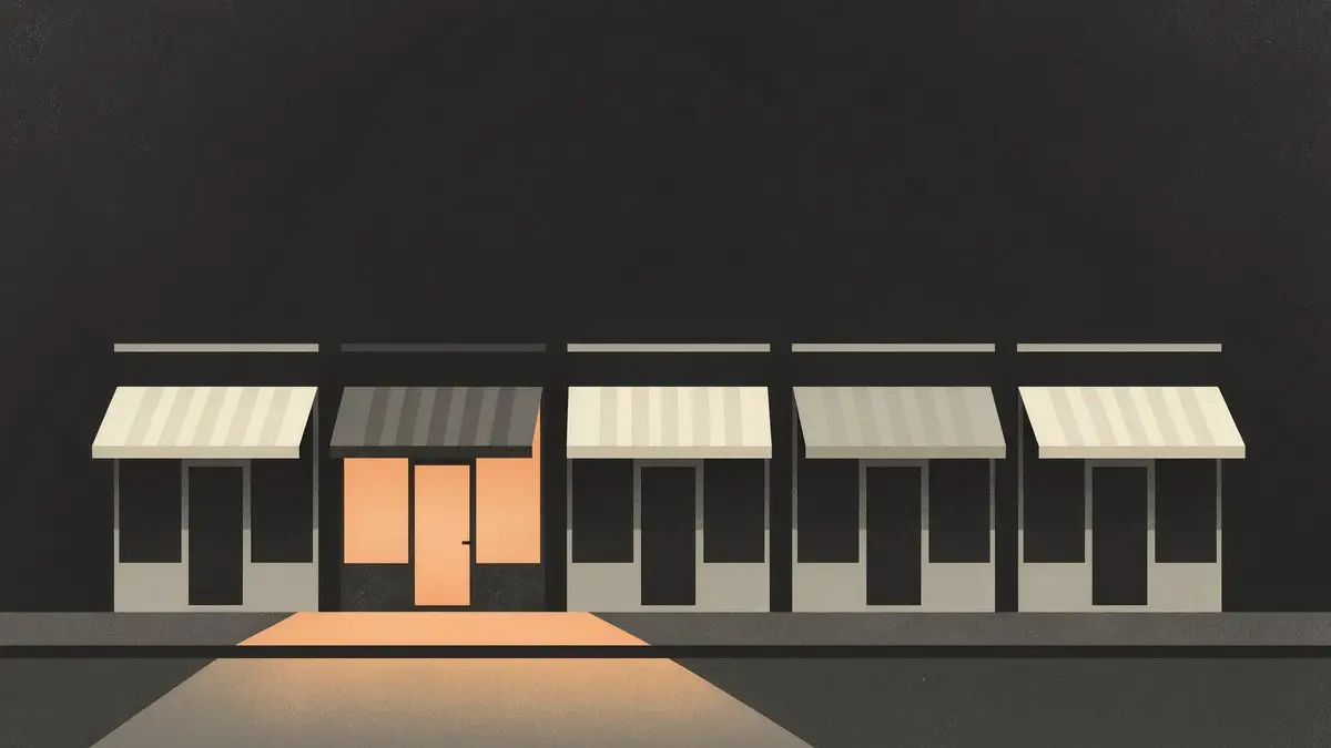 A dark row of storefronts at night, only one lit from within
