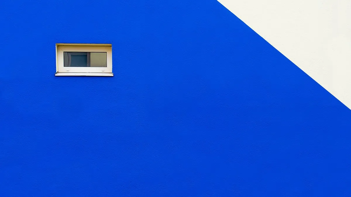 A minimalist design featuring a vibrant blue wall with a small, closed window.