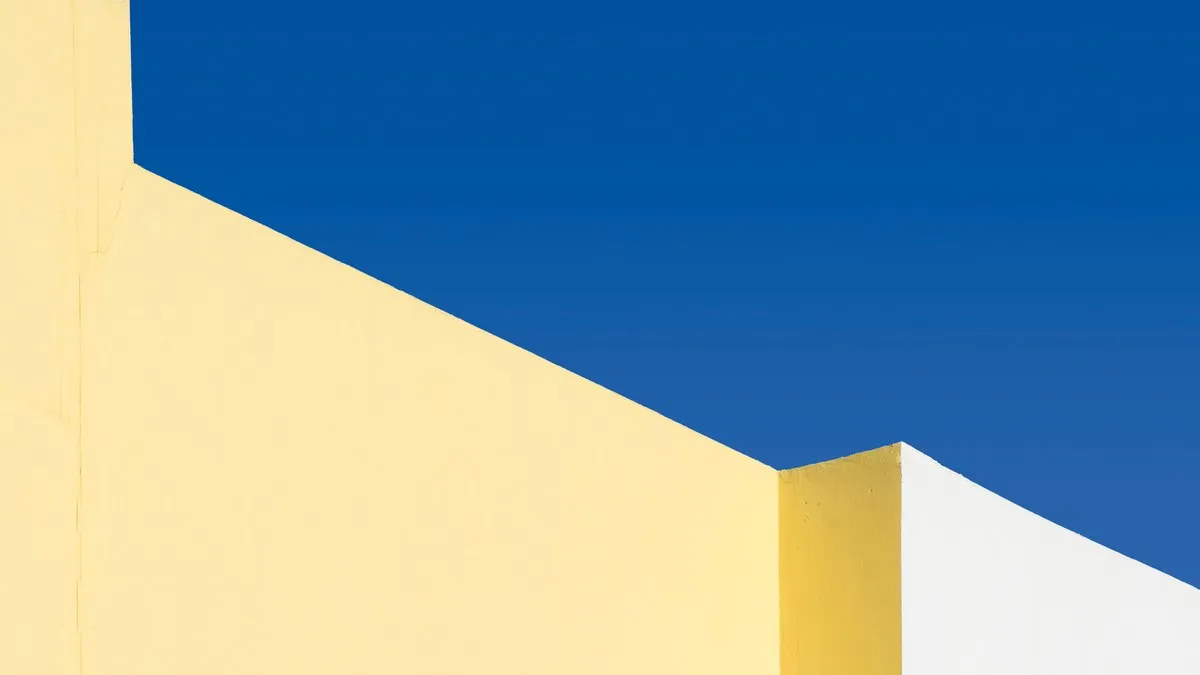 Abstract geometric yellow and white structures under a vibrant blue sky.