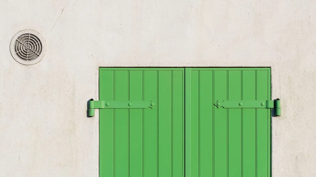 A green door with a rustic charm against a minimalist white wall, featuring a circular vent.