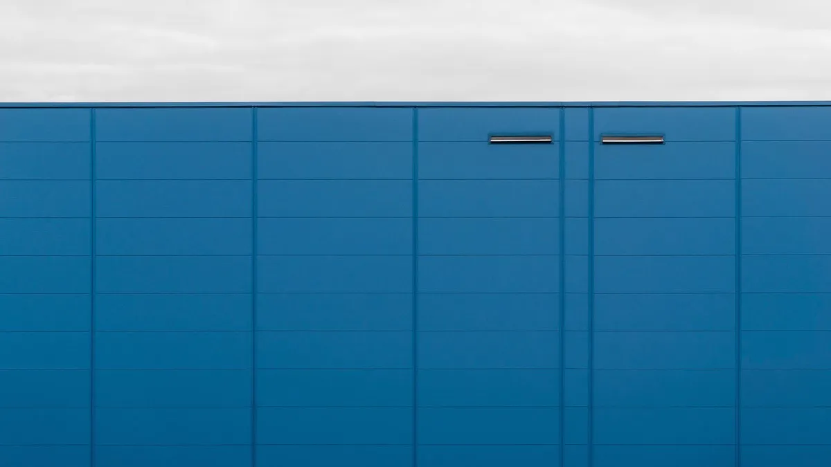 A modern blue building facade with clean lines and minimal design against a cloudy sky.