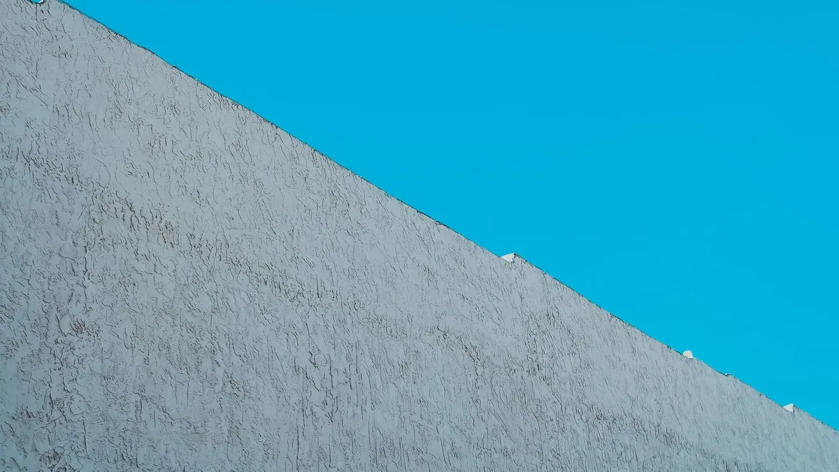 Low angle view of a white concrete wall against a clear blue sky, showcasing texture and minimalism.
