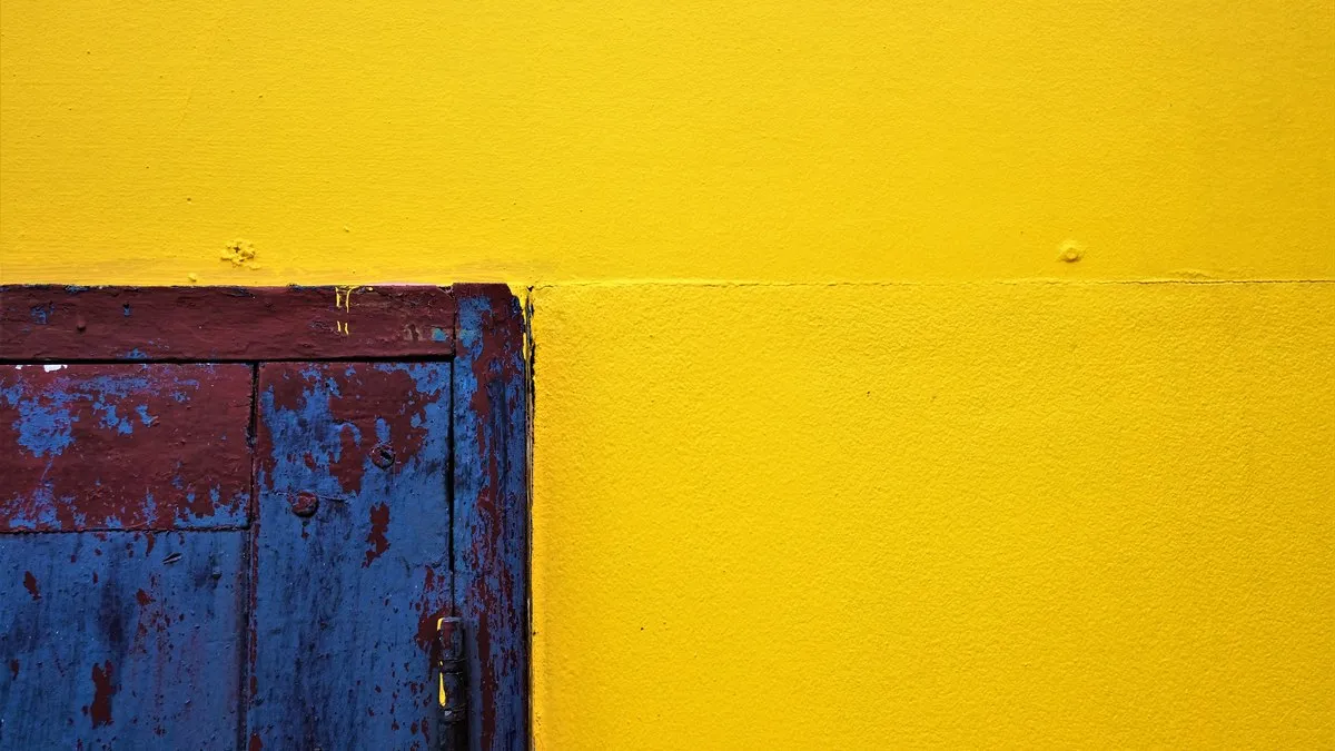 Close-up of a vibrant yellow wall paired with a rustic, textured blue door, showcasing vivid contrast.