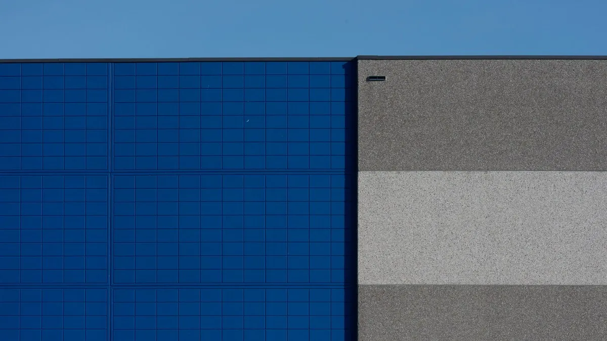 A minimalist building facade featuring a striking blue panel against a concrete gray wall under a clear sky.