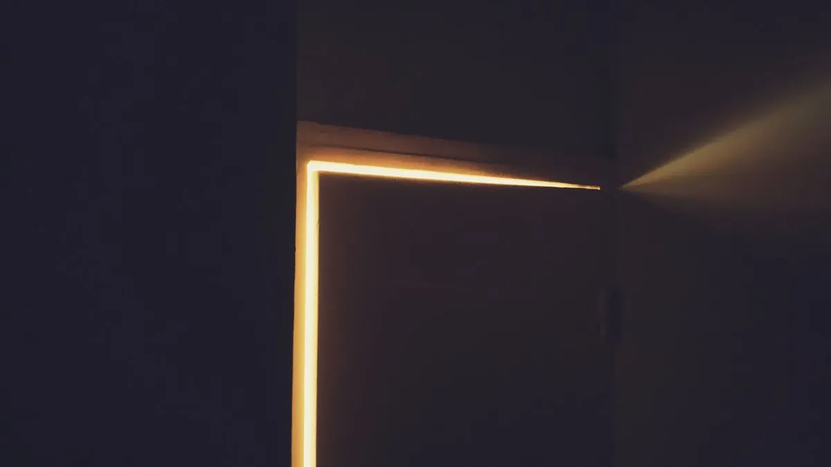 Beam of warm light coming through doorway with closed door into dark room