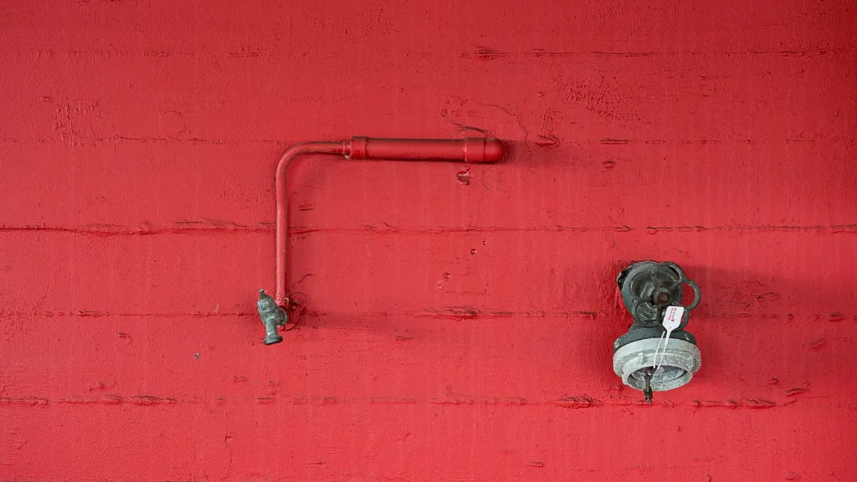Close-up of a red wall featuring an industrial faucet and pipeline. Minimalist design.