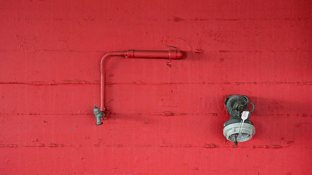 Close-up of a red wall featuring an industrial faucet and pipeline. Minimalist design.