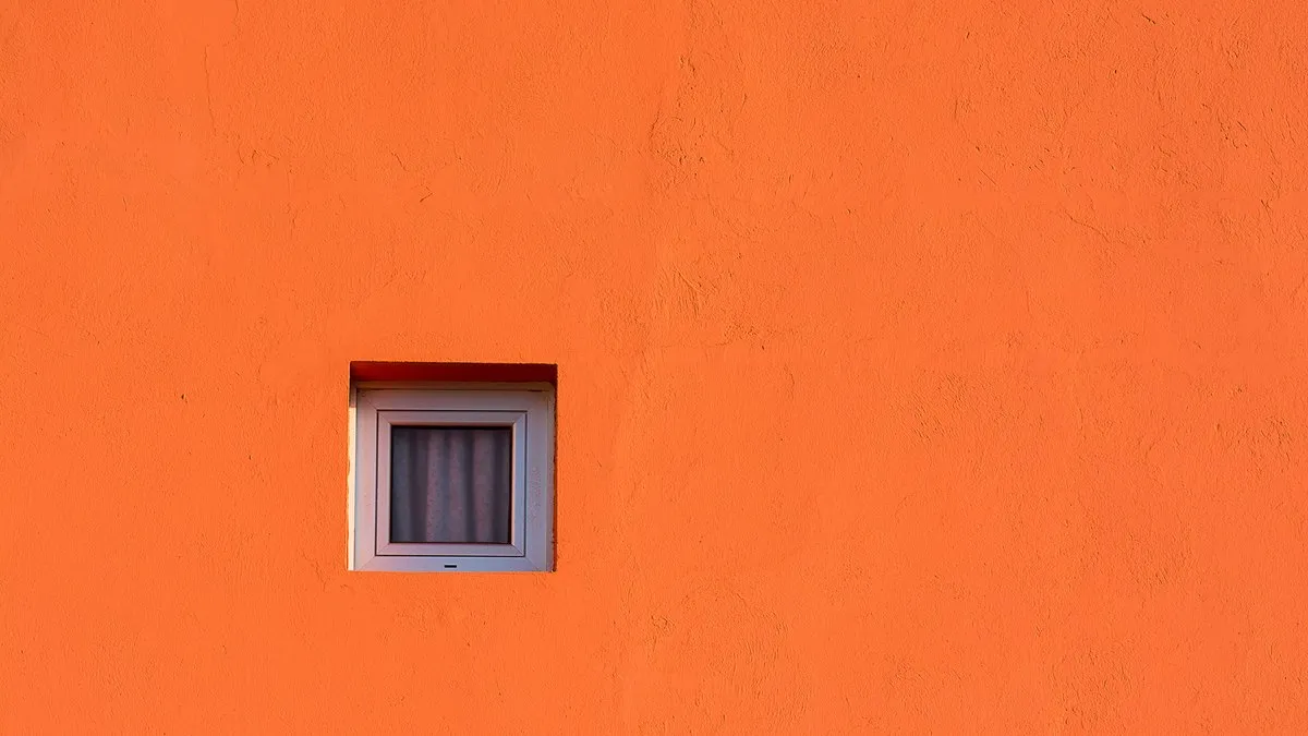 A vibrant orange wall featuring a small square window. Ideal for backgrounds or designs.