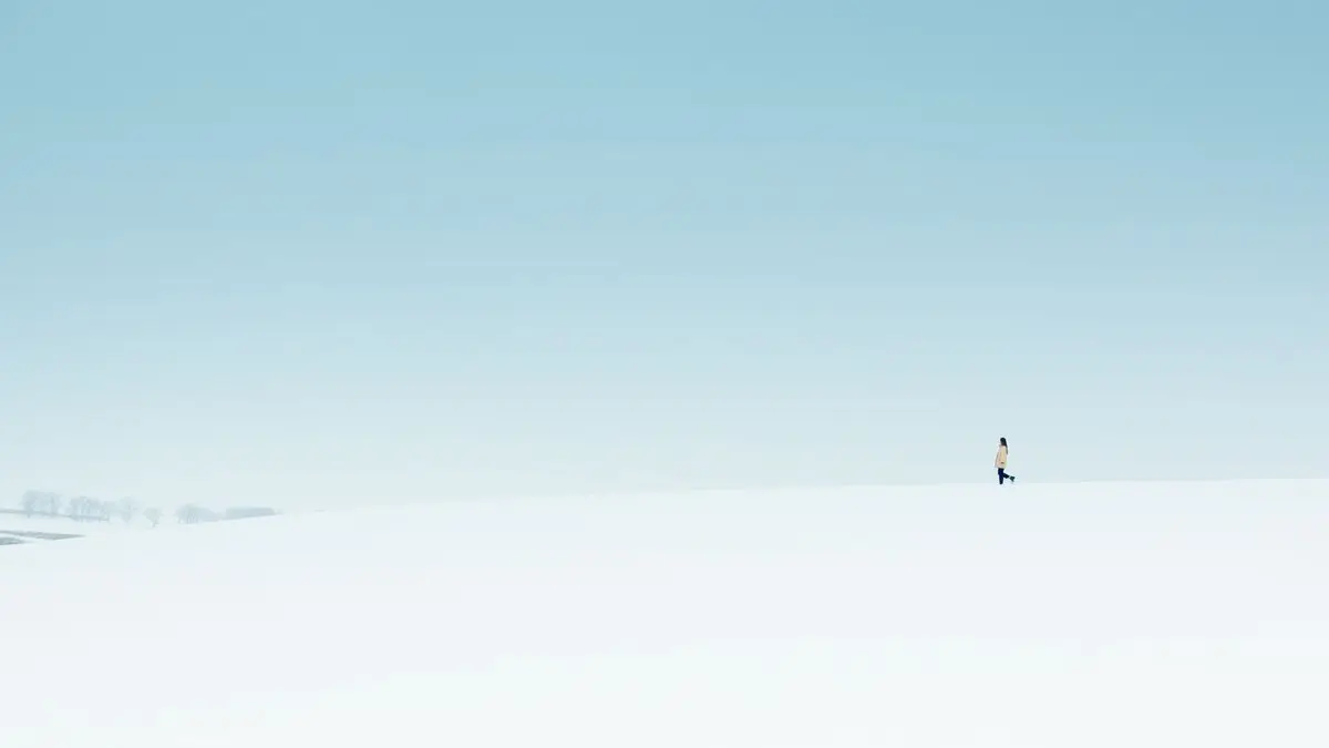 A lone figure walks on a vast snow-covered landscape under a clear sky.