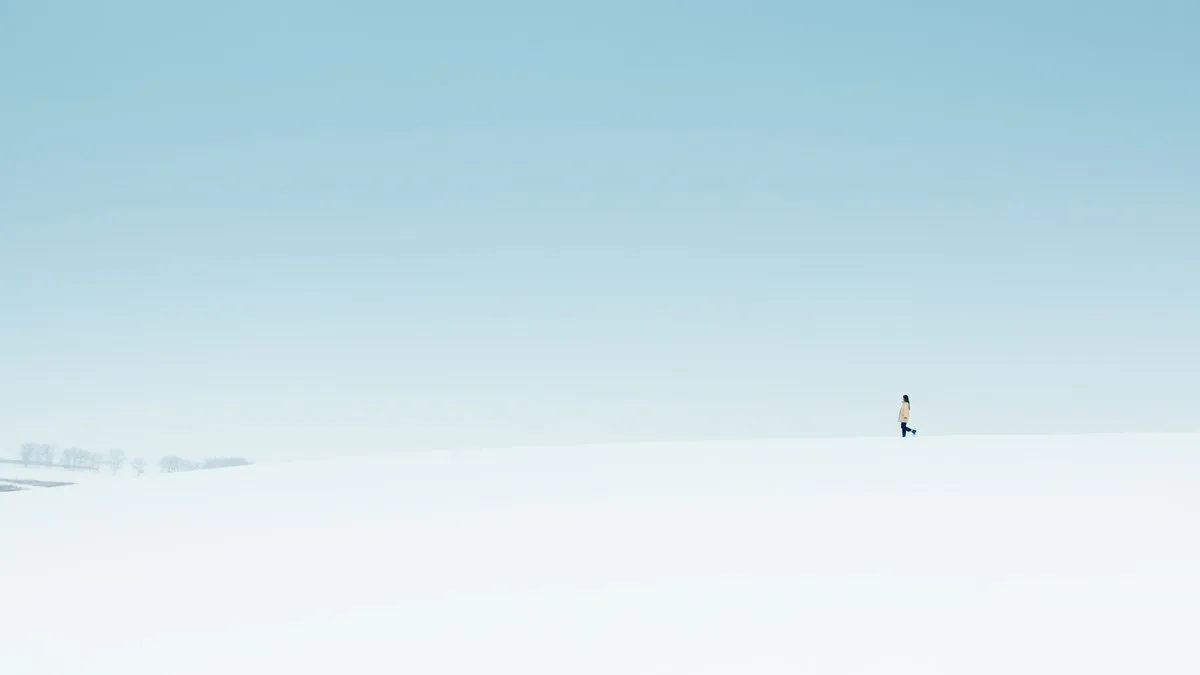 A lone figure walks on a vast snow-covered landscape under a clear sky.