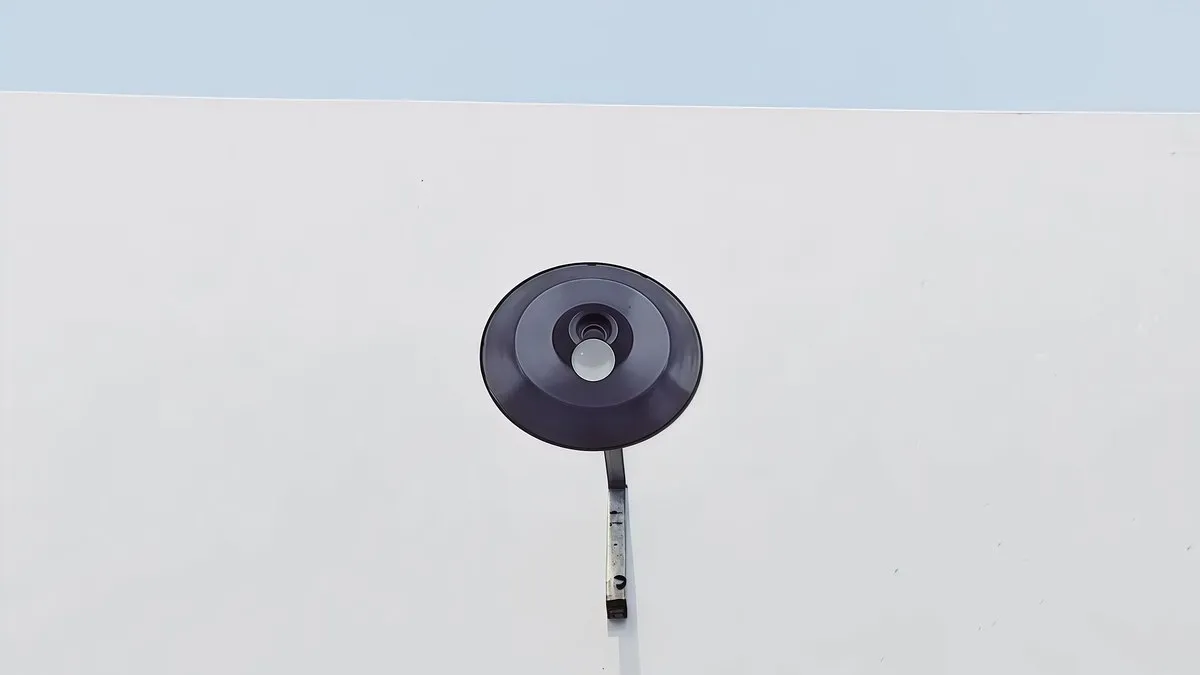 Abstract view of a minimalist wall-mounted black light fixture against a pale wall.