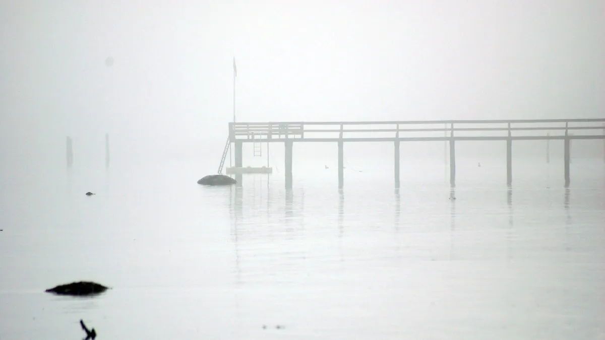A serene image of a wooden pier extending into foggy, still waters.