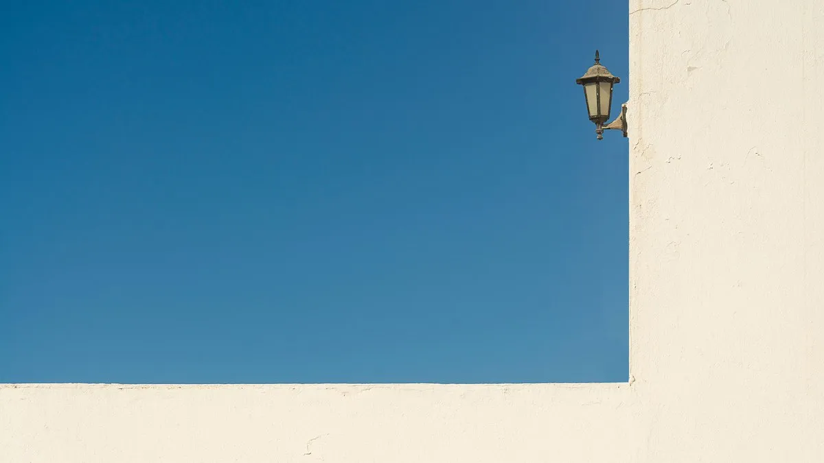 Minimalist photo of a blue sky with a white wall and an antique lantern, ideal for backgrounds.