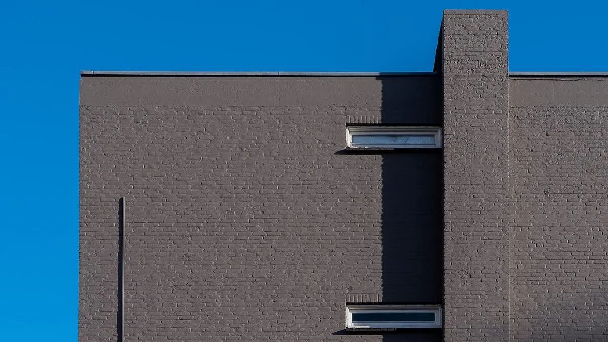A minimalist view of a grey brick building against a vibrant blue sky, highlighting architectural lines.