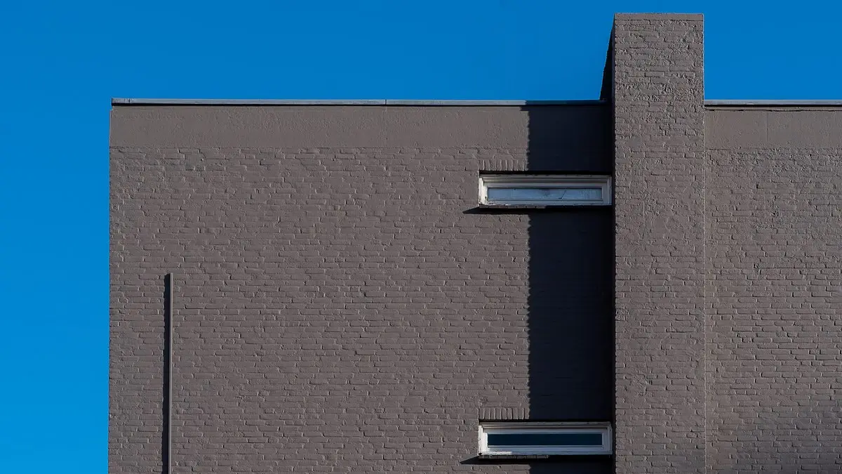 A minimalist view of a grey brick building against a vibrant blue sky, highlighting architectural lines.