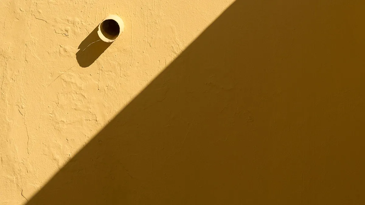 A sunlit yellow wall with a pipe casting a shadow, highlighting its texture.