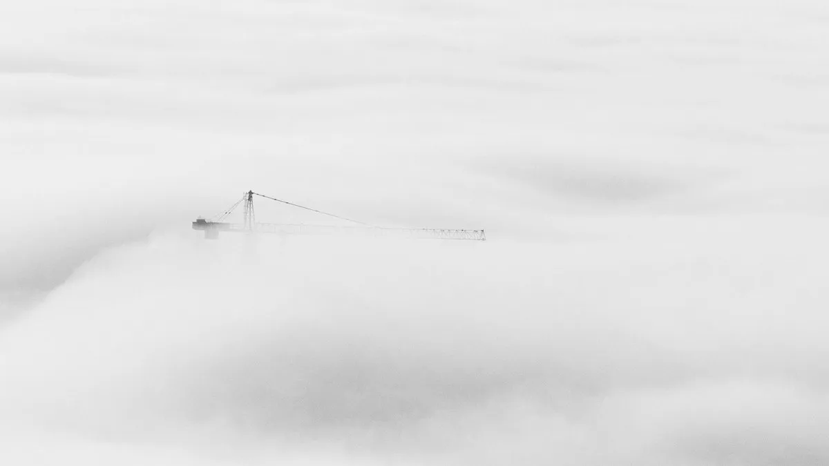 Ethereal view of a crane breaking through dense fog in Dubai, showcasing urban construction.