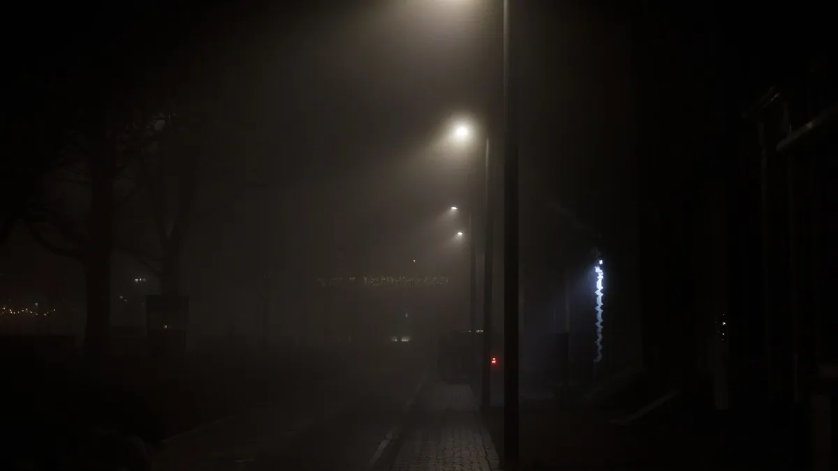A foggy urban street at night with streetlights creating a moody ambiance.