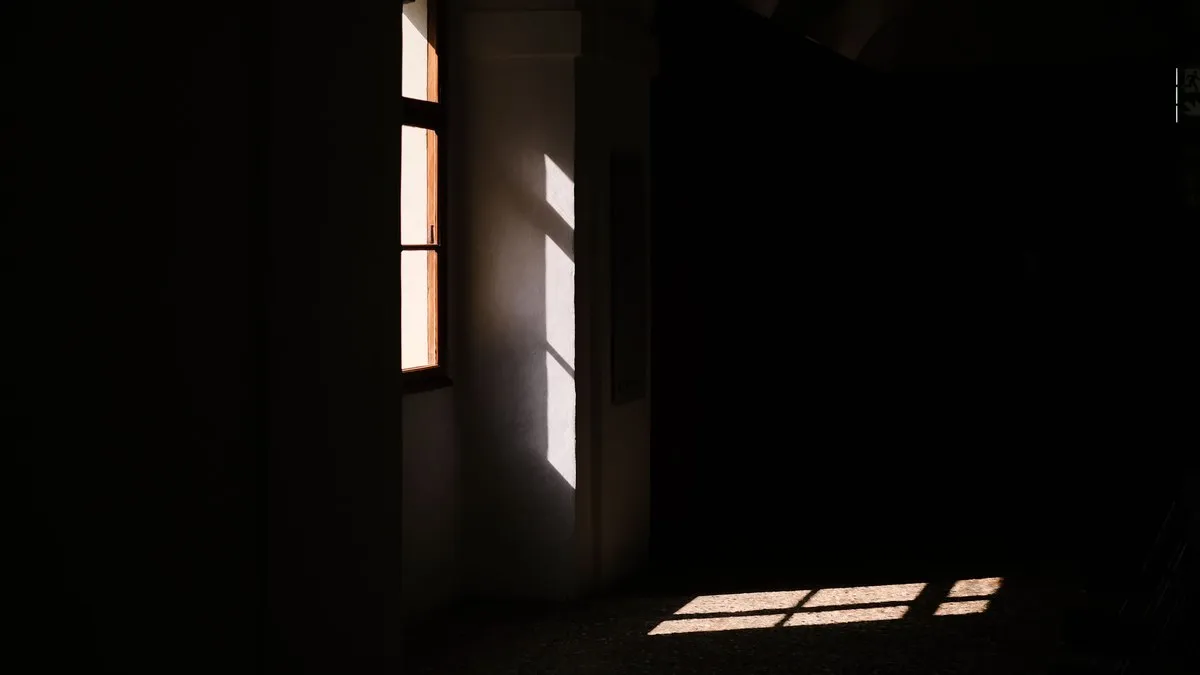 A dark room with sunlight streaming through a window, creating dramatic shadows.