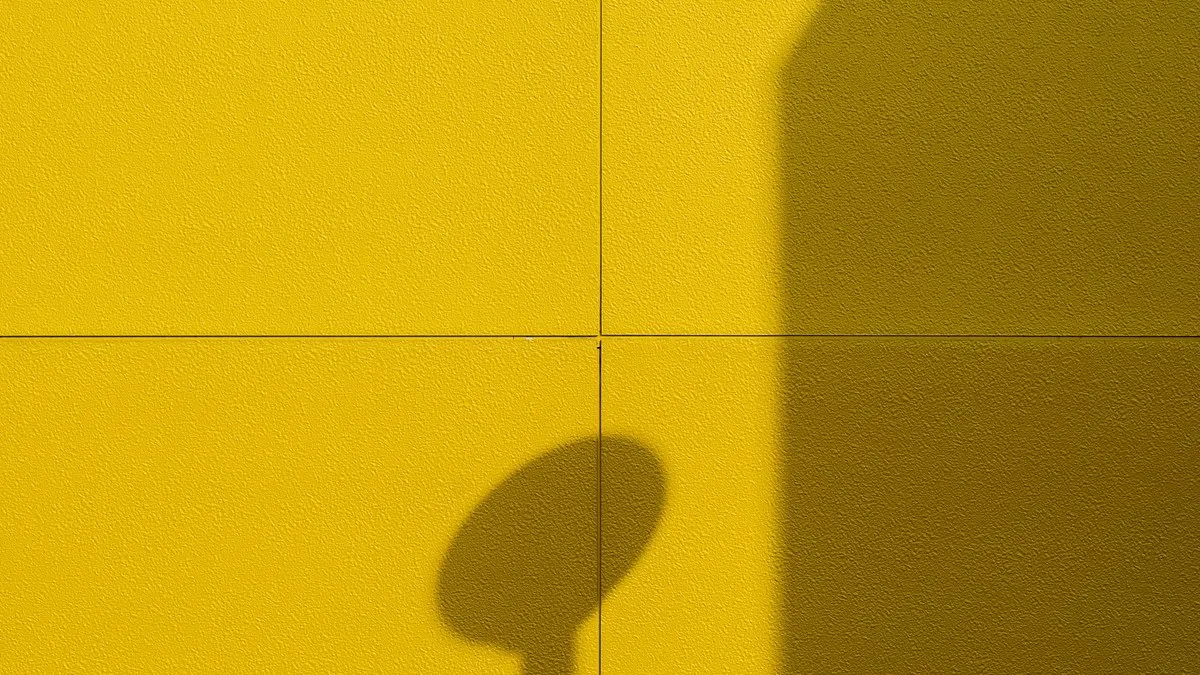 A minimalist shot of a yellow wall with distinct shadows casting a geometric pattern.