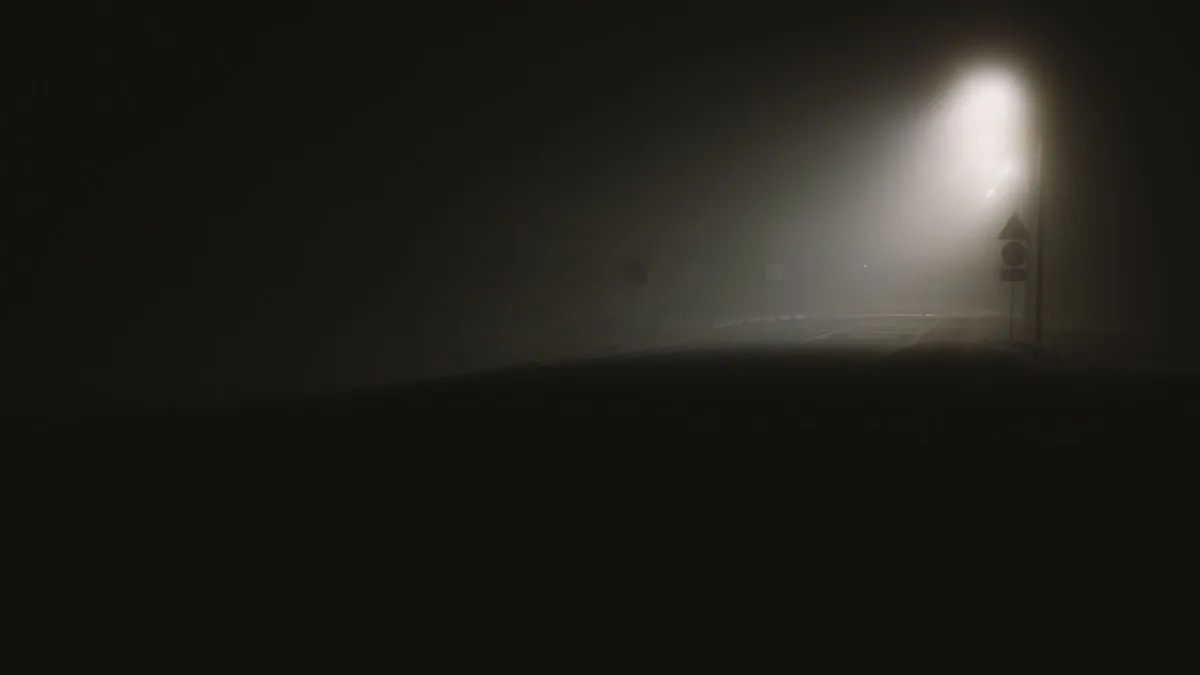 A fog-covered dark street illuminated by a single streetlight, creating an eerie night scene.