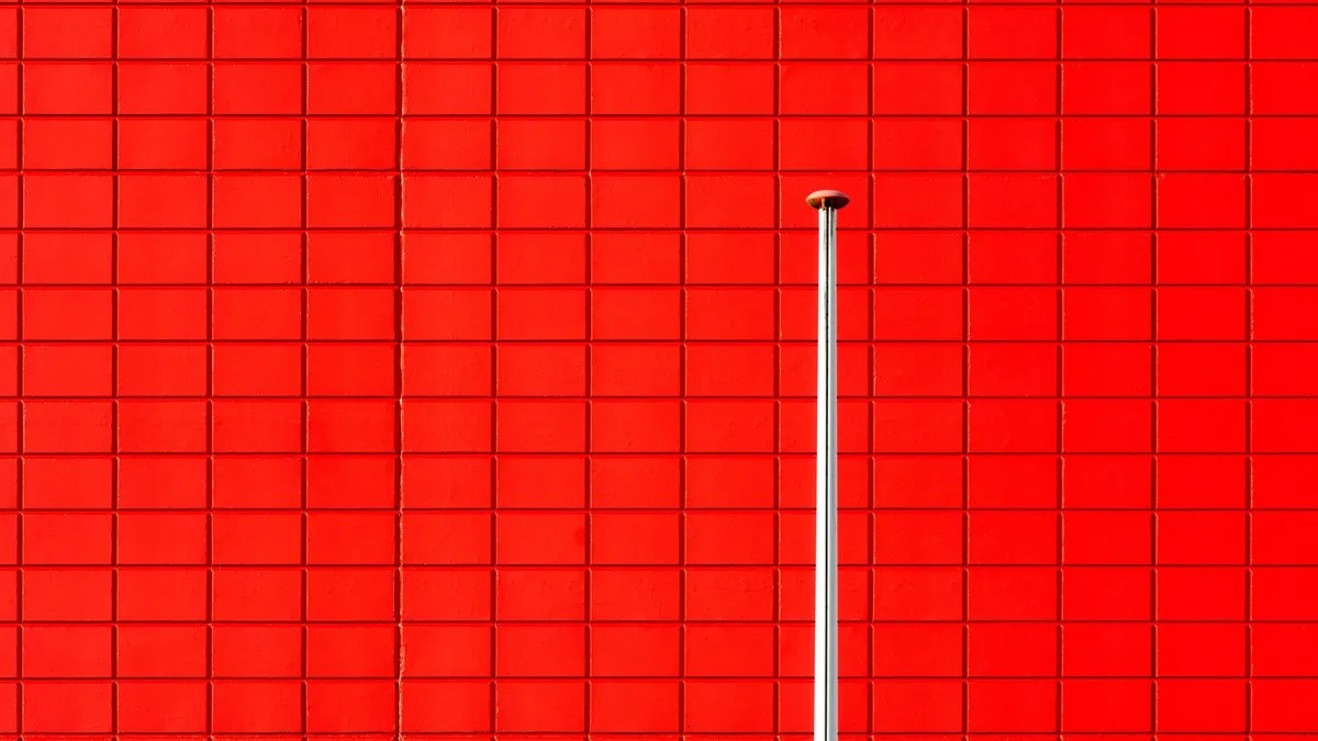 A striking red wall with a single vertical pole in a minimalistic design.
