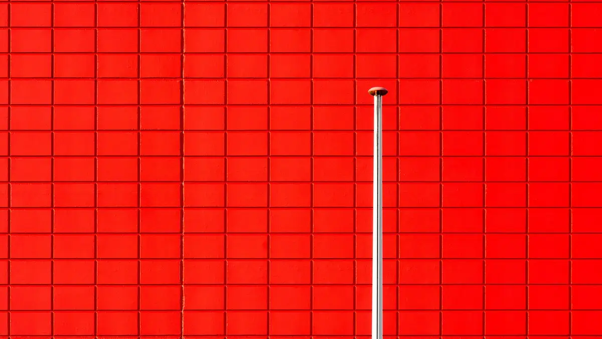 A striking red wall with a single vertical pole in a minimalistic design.