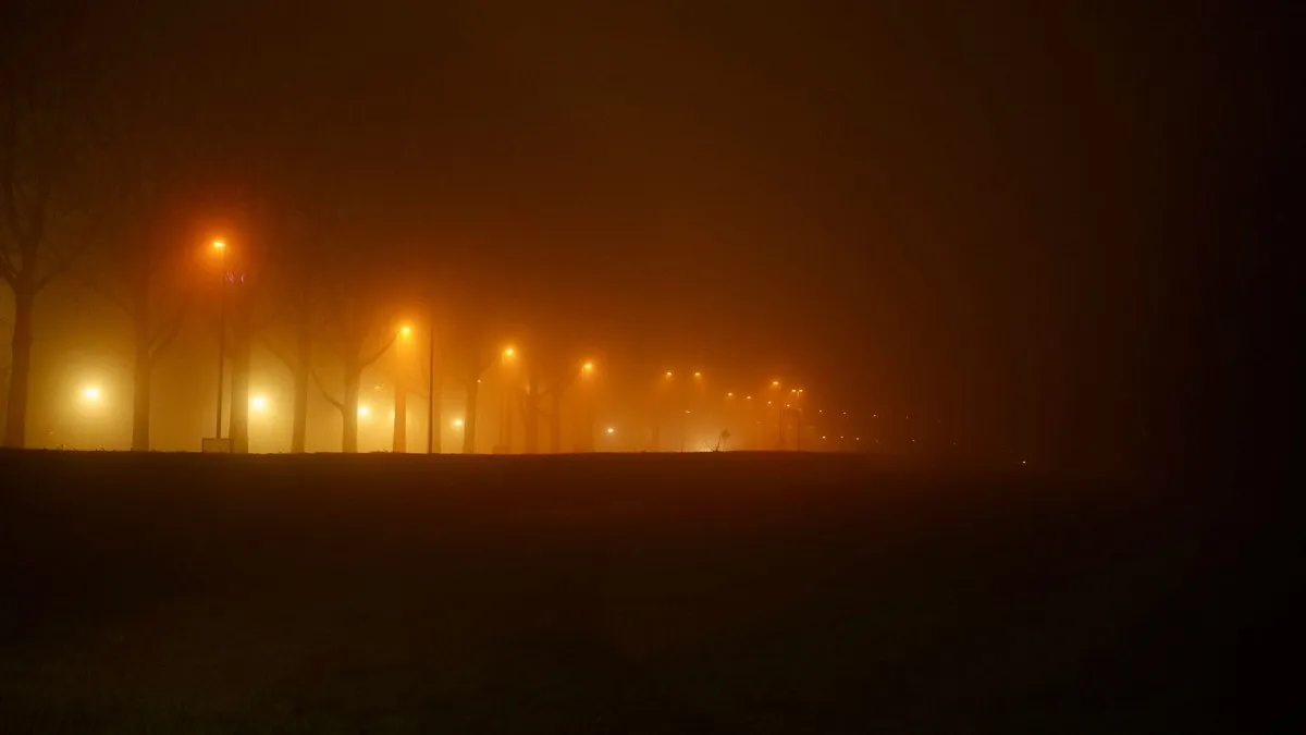 A foggy night scene with park lights and misty atmosphere along a deserted pathway.