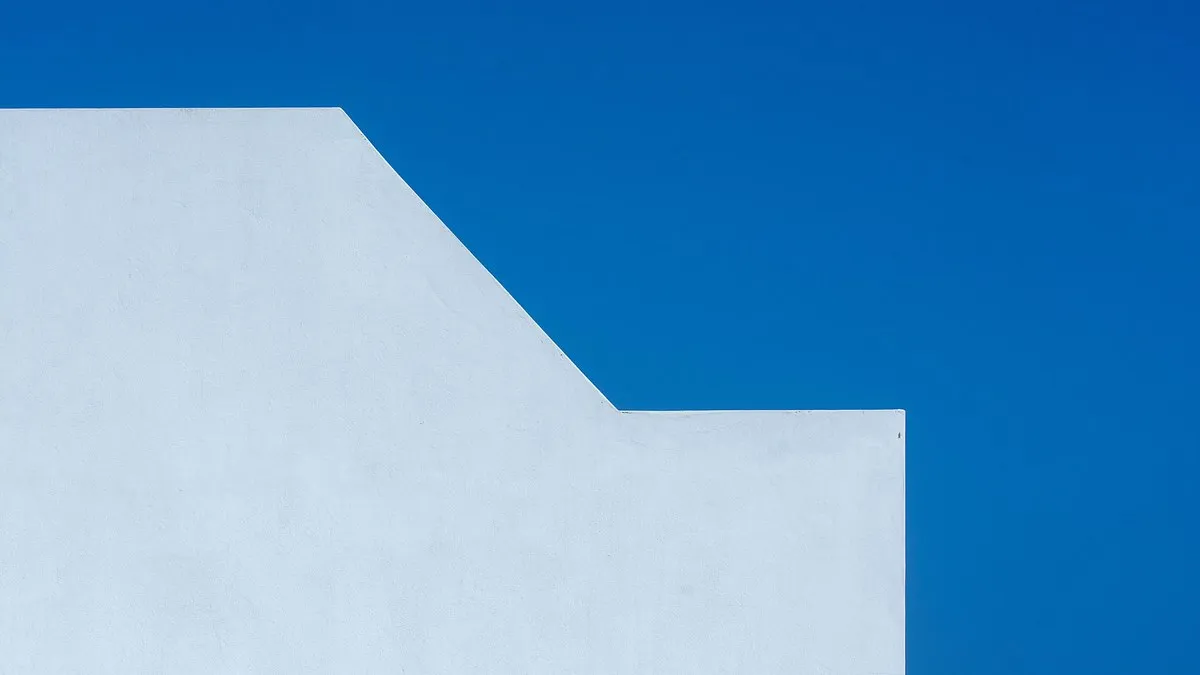 A minimalist photo of a white wall contrasting with a vibrant blue sky, showing geometric simplicity.