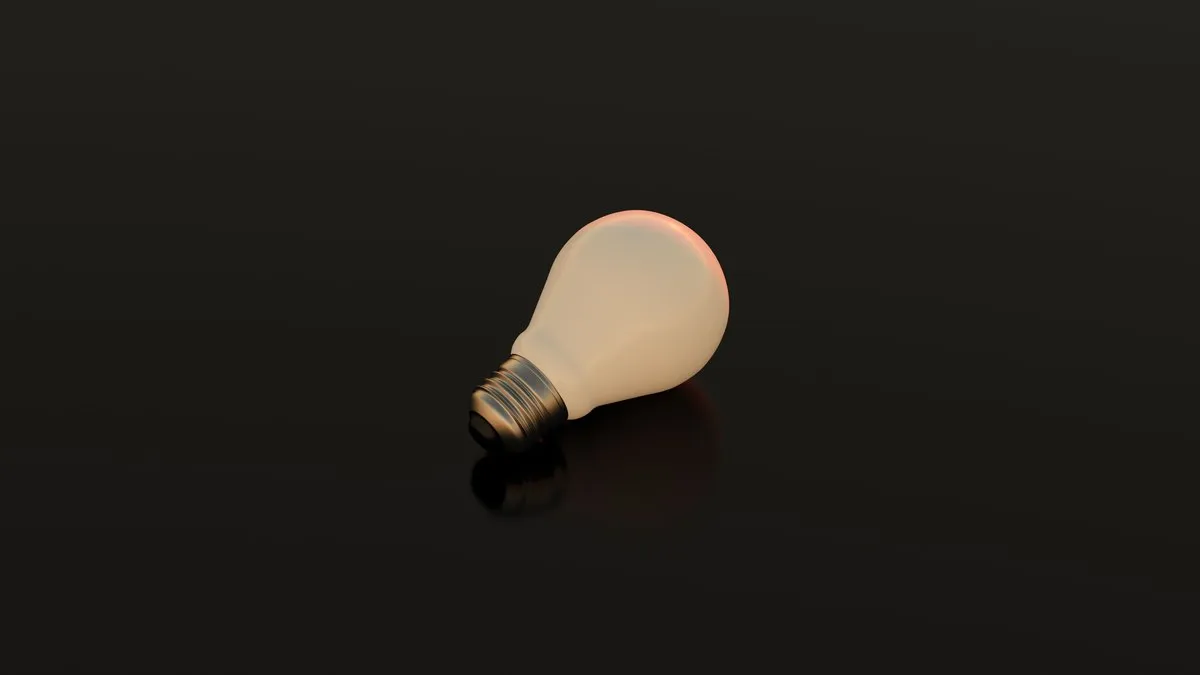 Simple ivory light bulb resting on a dark reflective surface, conveying innovation.