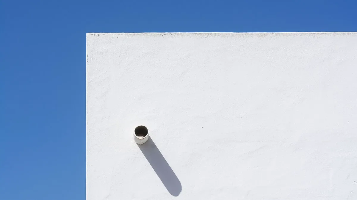 A minimalist white wall casting a distinct shadow under a clear blue sky, showcasing modern architectural design.