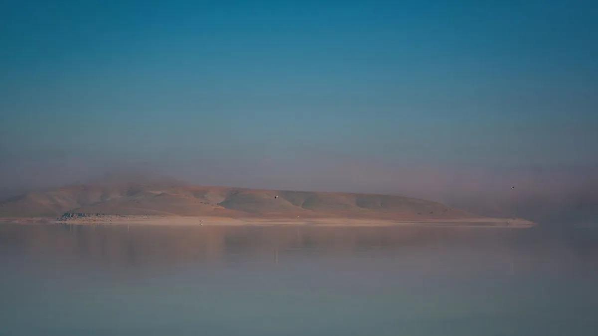Peaceful misty landscape over calm water reflecting mountains at dawn.