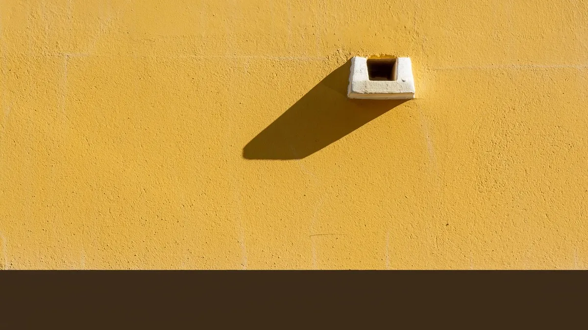 Close-up of a yellow painted wall with a sharp shadow, creating a minimalist urban aesthetic.