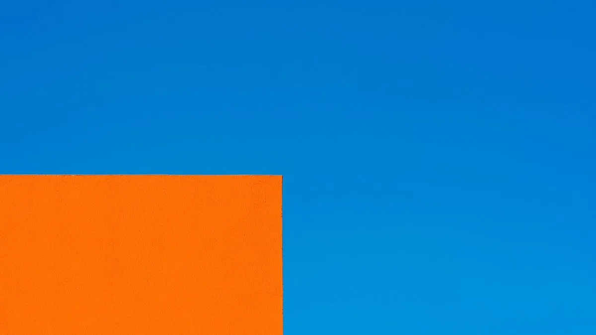 Bright orange geometric building corner set against a clear, vibrant blue sky.
