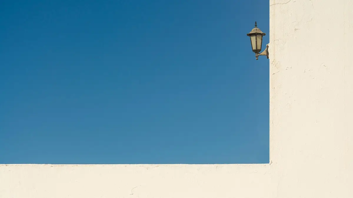 Minimalist photo of a blue sky with a white wall and an antique lantern, ideal for backgrounds.