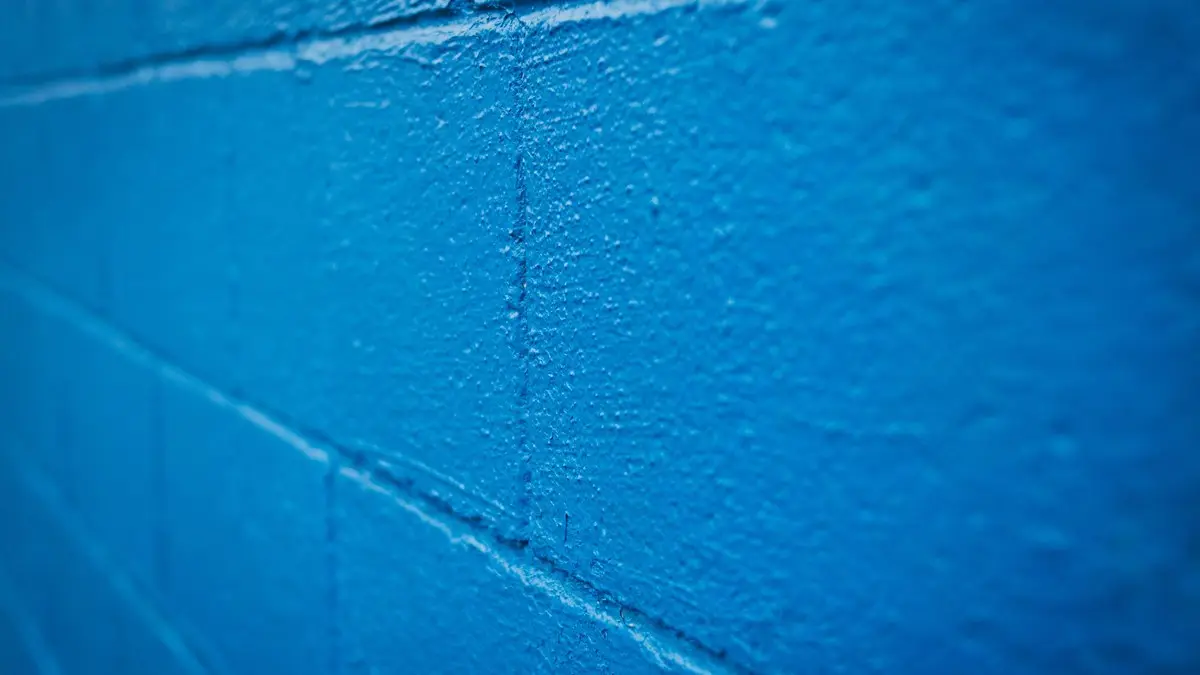 Uneven surface of rough brick wall painted in bright blue color in selective focus
